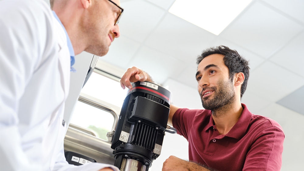 A nephrologist in a white lab coat and a technician in a red polo shirt examining a pump of the water treatment system AQUAboss nX.