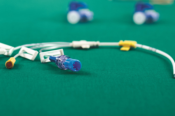 Central venous catheter Certofix® Trio with white fixation clamps lying on green surgical drape.