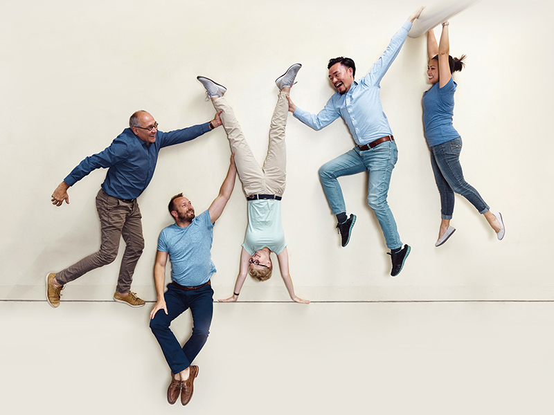 Five people striking different poses, with one person being held upside down by the others.