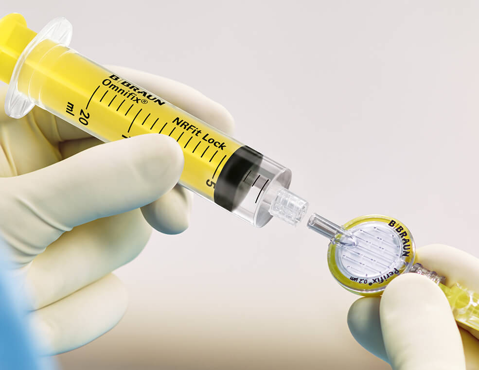 Gloved hands connecting a yellow Omnifix syringe with NRFit lock to a Perifix filter and catheter connector for regional anesthesia